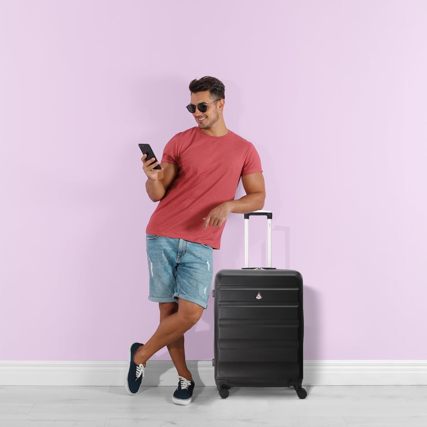 Man with black Aerolite suitcase against pink wall
